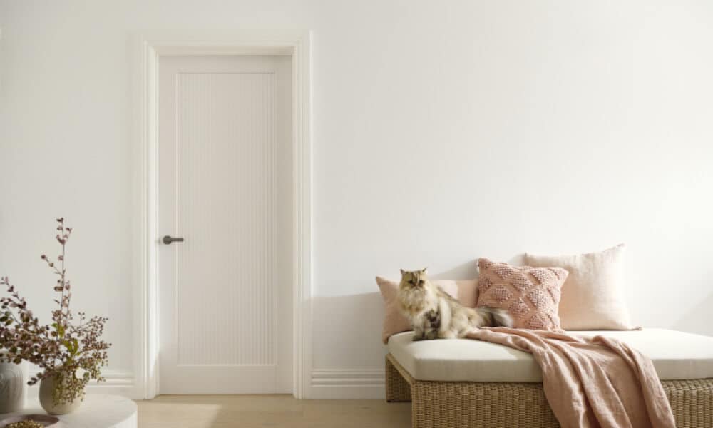 A photo of a room. A cat sits on a sofa and there is a door next to it.