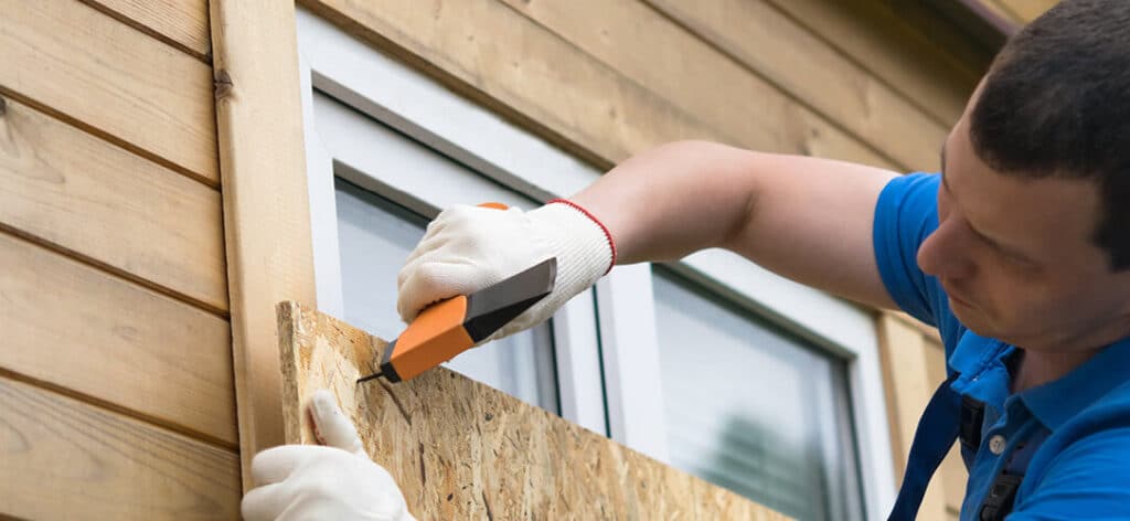 A man covering his windows with plywood