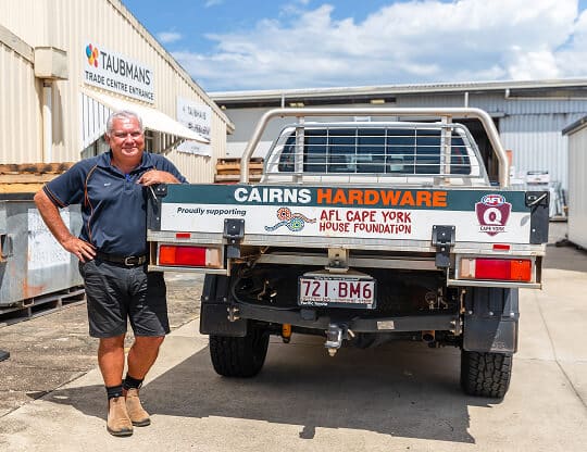 A Cairns Hardware employee smiling to camera beside a company-branded ute.